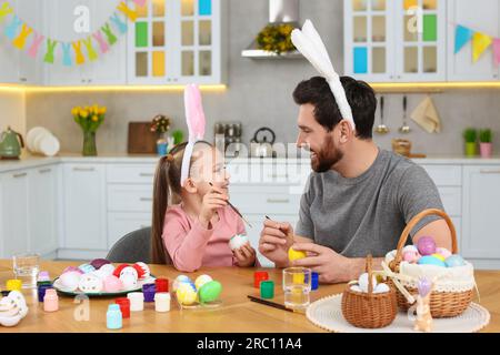 Father and his cute daughter painting Easter eggs at table in kitchen Stock Photo