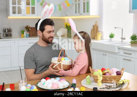 Father and his cute daughter with wicker basket full of Easter eggs in kitchen Stock Photo