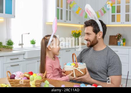 Father and his cute daughter with wicker basket full of Easter eggs in kitchen Stock Photo