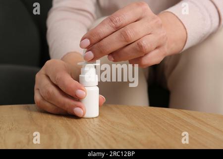 Woman opening nasal spray at wooden table indoors, closeup Stock Photo
