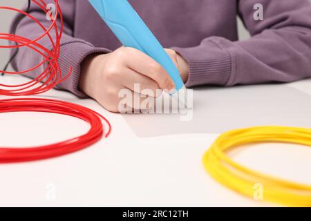 Boy drawing with stylish 3D pen at white table, closeup Stock Photo