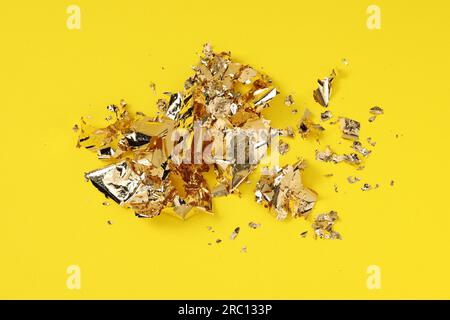 Many pieces of edible gold leaf on yellow background, above view Stock Photo