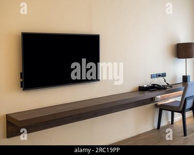 Mockup blank space on smart TV black screen over the empty long brown walnut wooden table shelf with chair at working area on white wall background wi Stock Photo