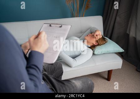 Psychological treatment concept. Professional handsome young psychologist helping his patient while having a session with her, taking notes about Stock Photo