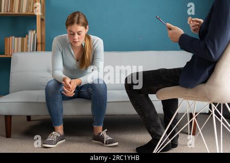 Psychologist taking notes during therapy session with sad young woman in his office Stock Photo