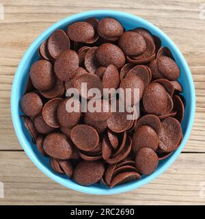 Directly above view of glazed corn flakes in blue bowl on wooden background close-up Stock Photo