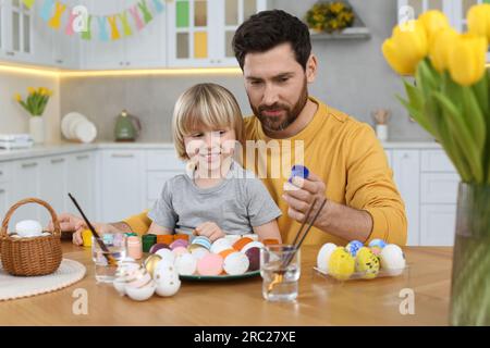 Father and his cute son painting Easter eggs at table in kitchen Stock Photo