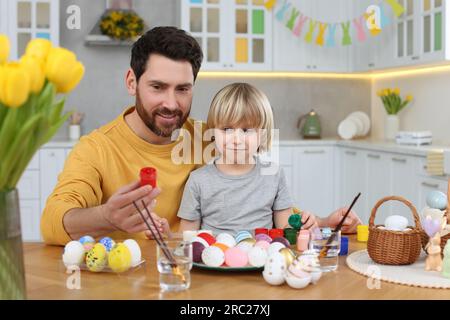 Father and his cute son painting Easter eggs at table in kitchen Stock Photo
