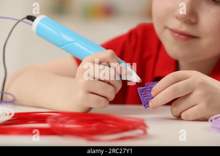 Boy drawing with stylish 3D pen at white table, closeup Stock Photo