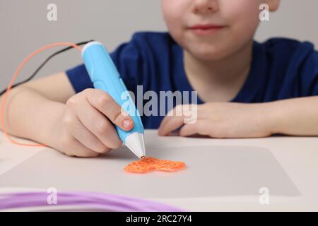 Boy drawing with stylish 3D pen at white table, closeup Stock Photo