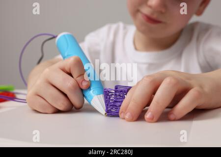 Boy drawing with stylish 3D pen at white table, closeup Stock Photo