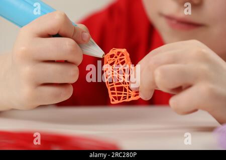 Boy drawing with stylish 3D pen at white table, closeup Stock Photo