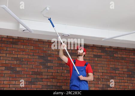 Handyman painting ceiling with roller in room Stock Photo