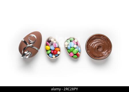 Delicious chocolate eggs, paste and colorful candies on white background, flat lay Stock Photo