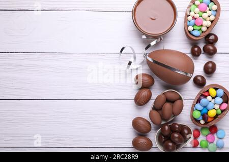 Delicious chocolate eggs, paste and candies on white wooden table, flat lay. Space for text Stock Photo