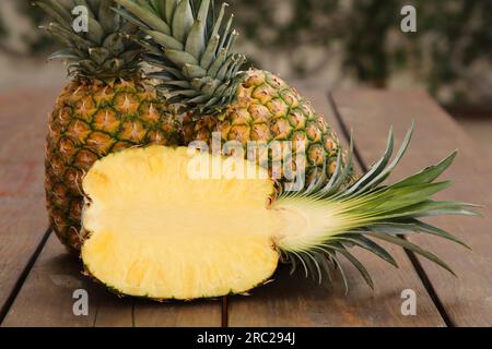 Whole and cut ripe pineapples on wooden table, closeup Stock Photo