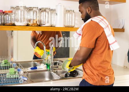 Focused african american man with towel on arm washing dishes in kitchen Stock Photo