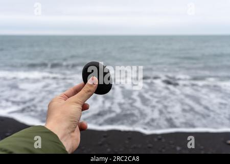 Hand holding black pebble at Reynisfjara Black Sand Beach In Iceland Stock Photo