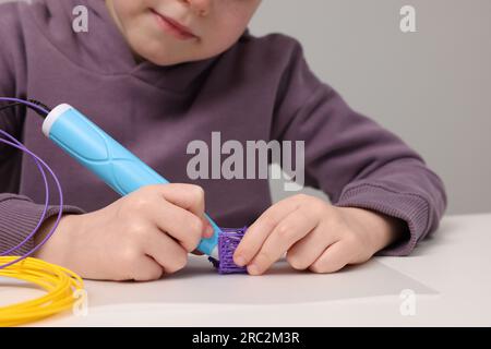 Boy drawing with stylish 3D pen at white table, closeup Stock Photo
