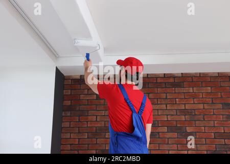 Handyman painting ceiling with roller in room, back view Stock Photo