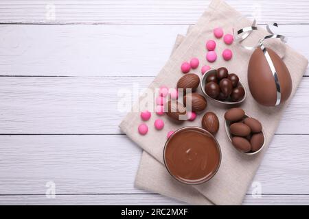 Delicious chocolate eggs, paste and candies on white wooden table, flat lay. Space for text Stock Photo