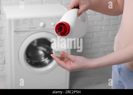 Woman pouring fabric softener from bottle into cap for washing clothes indoors, closeup Stock Photo