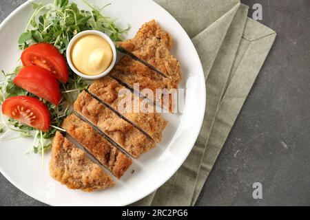 Tasty cut schnitzel served with sauce, microgreens and tomato on grey textured table, top view. Space for text Stock Photo