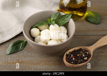 Tasty mozarella balls, basil leaves, oil and spices on wooden table Stock Photo