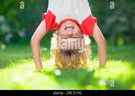 Little boy hanging upside down. Handstand exercise for little kids. Active child playing on sunny garden lawn. Summer fun. Kids play outdoor. Stock Photo