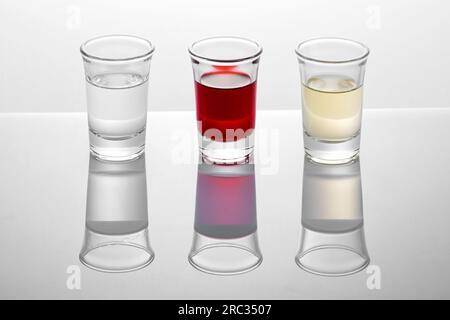 Shot glasses with red white and transparent alcoholic drinks reflecting on surface in studio Stock Photo
