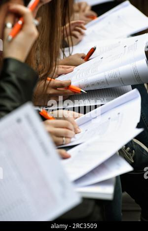 High angle group of crop unrecognizable students sitting at table with pens and papers and doing test during studies Stock Photo