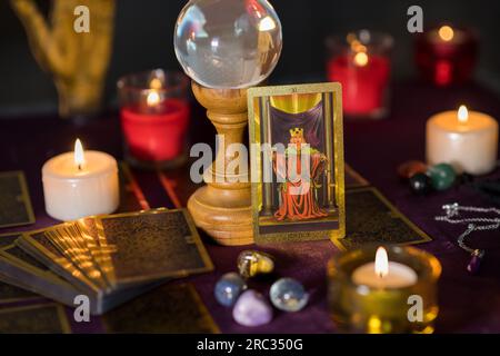 Justice tarot card with deck of cards placed on table near set of burning candles with glass crystal ball and stones Stock Photo