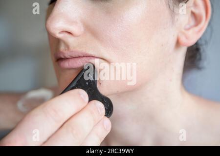 Young Caucasian woman getting facial treatment. Therapist doing skin scrape technique. Chinese technique, gua sha, for pain relief and treatment Stock Photo