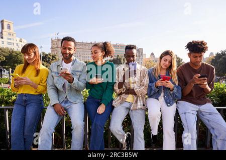 Multiethnic group of friends sitting outside using mobile phone.  Stock Photo