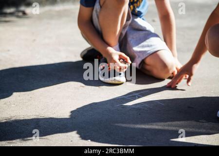 Happy childhood. Caucasian children playing outside during the day, scratching the ground with a rock to play the classic game of tic-tac-toe. Stock Photo