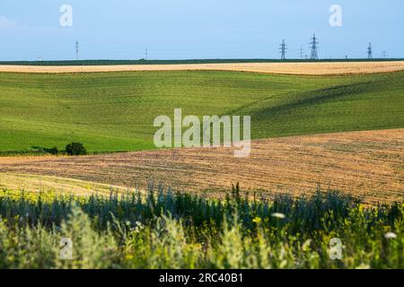 Endless farm fields on the slopes of the hills are sown with various crops. Peaceful rural landscape. Summer evening in the western Ukraine near Rivne Stock Photo