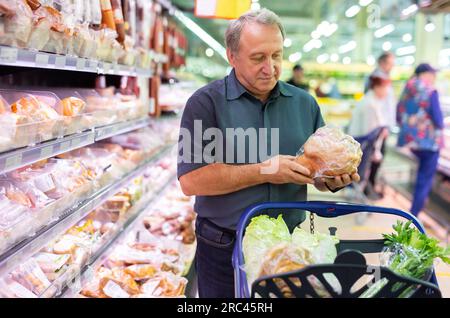 Elderly man chooses chicken meat in supermarket Stock Photo