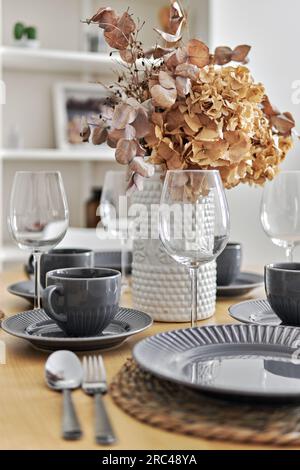 Pretty flowers in vase on a dinning table with served coffee or tea cups and plates is ready for quests reception or family breakfast, close up shot, Stock Photo