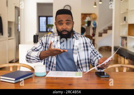 Portrait of focused african american man having video call and holding document at home Stock Photo