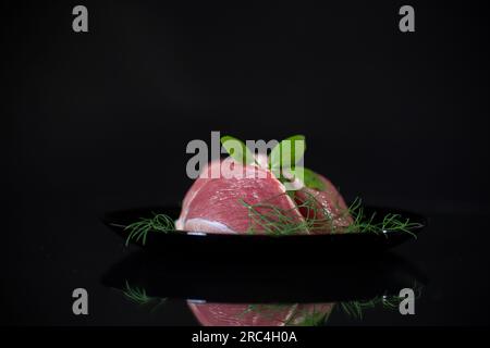 a piece of fresh pork meat in a plate, isolated on a black background. Stock Photo