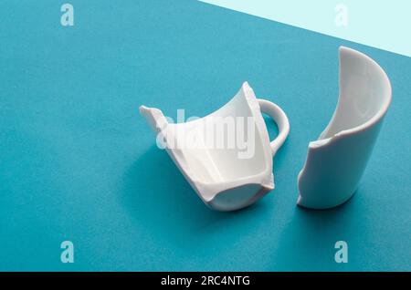 Detail of a broken cup on a blue background, representing vulnerability and disruption. Stock Photo