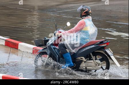 SAMUT PRAKAN, THAILAND, MAY 12 2023,  A driver of moto-taxi drives through a puddle in the rain Stock Photo