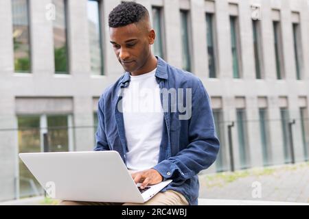 Concentrated African American male freelancer with portable computer browsing internet and looking at screen while working on remote project on street Stock Photo