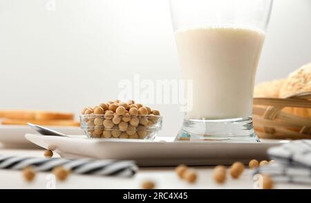Detail of soy drink in glass cup with soy beans in a bowl on wooden bench and white isolated background. Front view. Stock Photo