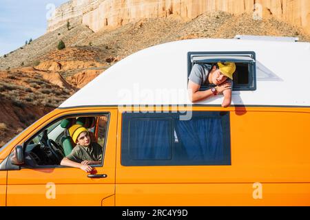 Male amputee in casual clothes with cap stretching hand through top window of yellow van with a child sitting inside looking at the camera Stock Photo
