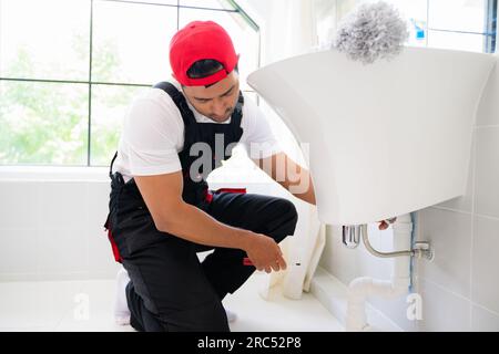 Repairman in black overalls repairing cabinet in kitchen at house, Technician examining oven with in kitchen, Maintenance and household service Stock Photo