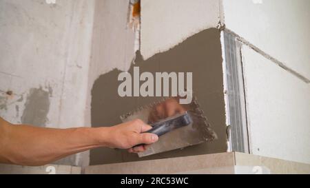 The adhesive solution is applied to the wall. Putty on the wall, for gluing ceramic tiles. Laying gypsum tiles on gypsum wall adhesive with a spatula Stock Photo