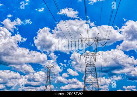 Horizontal shot of main electric towers against puffy white clouds in a blue sky. Stock Photo