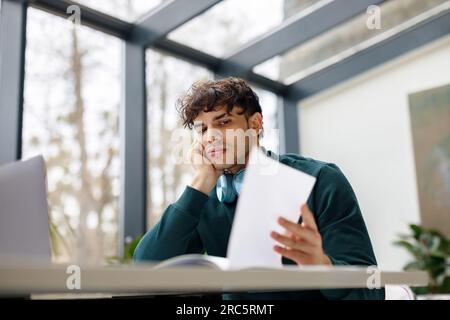 Portrait of bored european guy using laptop to write coursework paper, studying online, preparing for web exam Stock Photo