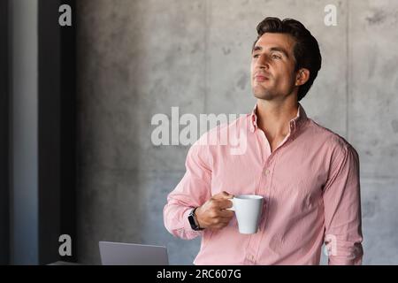 Handsome young businessman standing by workdesk, drinking coffee Stock Photo